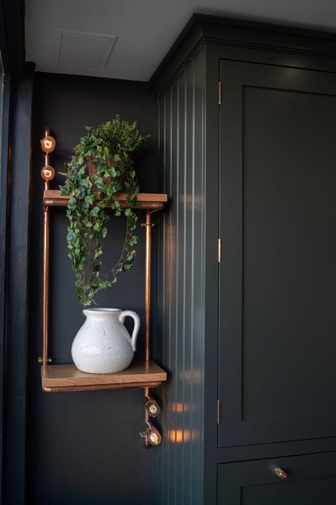 copper wall shelf, with white jug, and green plant.