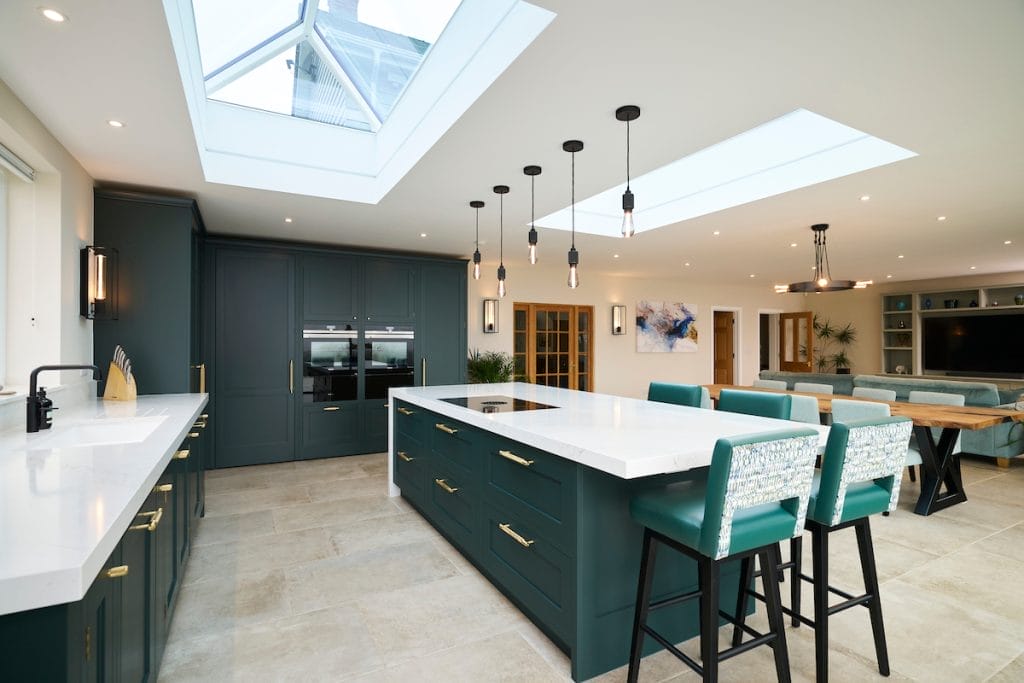 Luxury open-plan green shaker kitchen with large central island, brass handles, quartz worktops, and skylights – designed by The Essex Kitchen Design Company