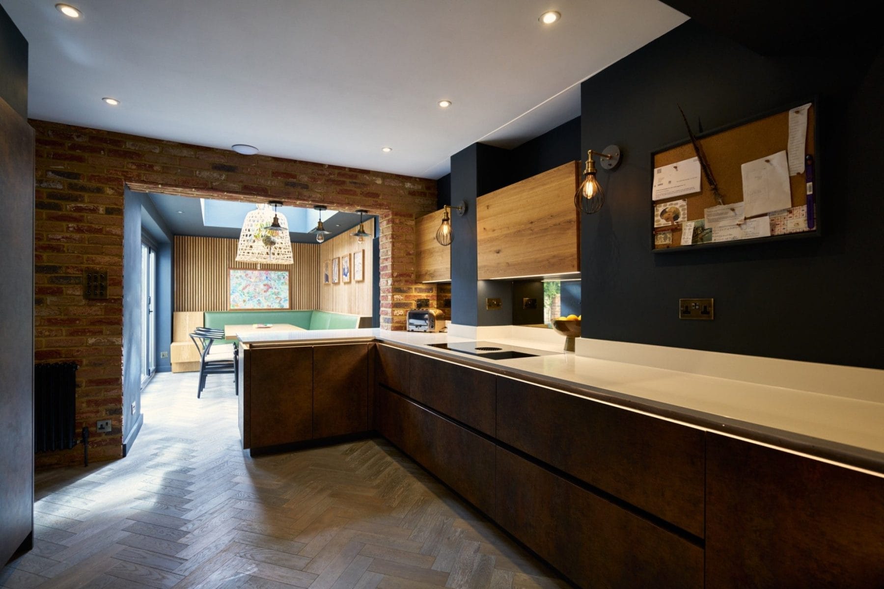 Contemporary handleless kitchen with breakfast bar in Essex featuring dark textured cabinetry, integrated lighting, and banquette seating
