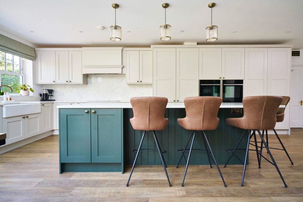 Two-tone shaker kitchen with sage green island, cream cabinetry, quartz worktops and leather bar stools – designed by The Essex Kitchen Design Company
