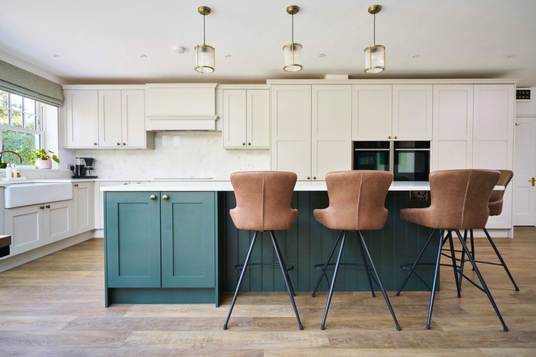 Two-tone shaker kitchen with sage green island, cream cabinetry, quartz worktops and leather bar stools – designed by The Essex Kitchen Design Company