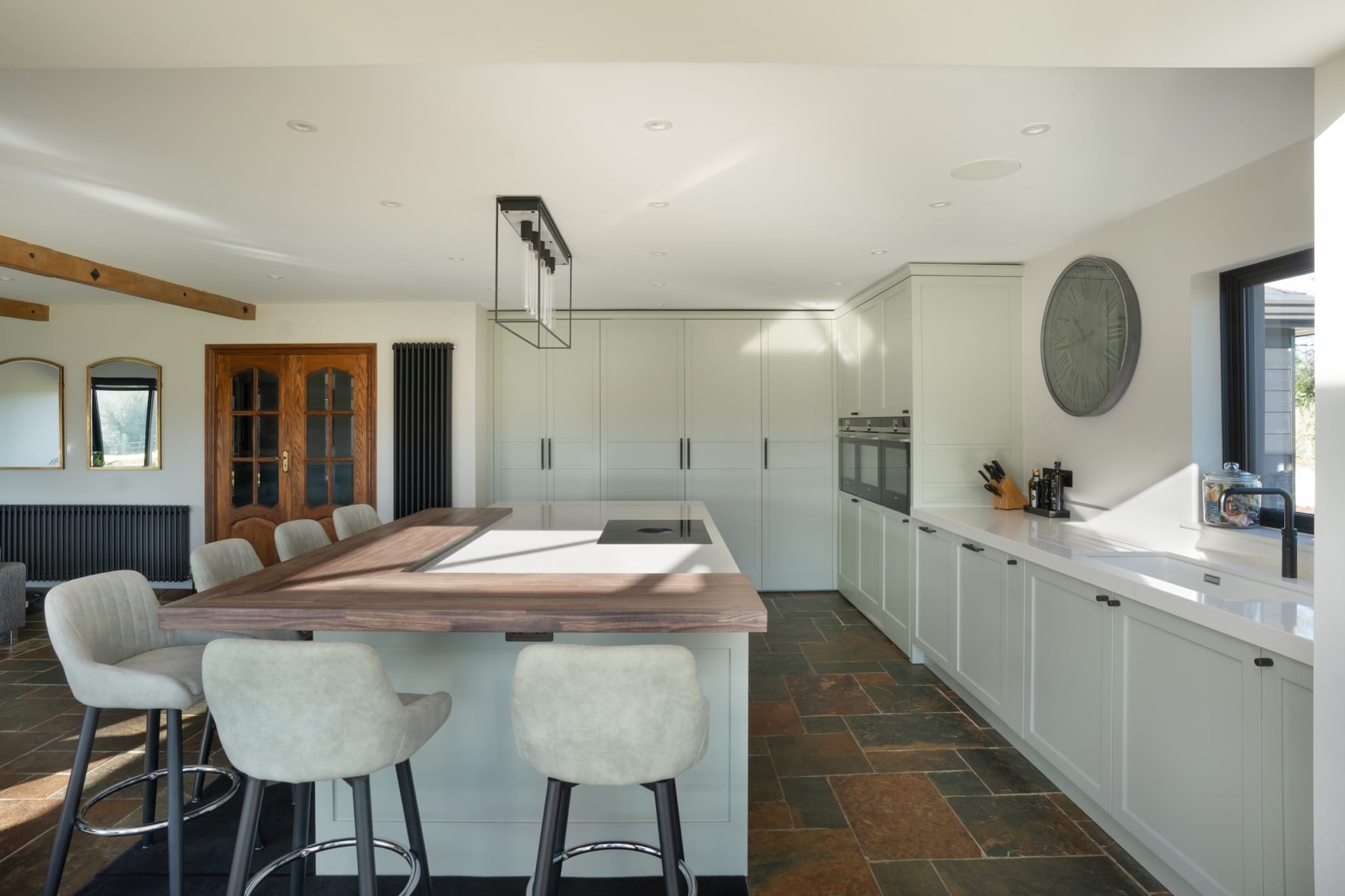 Pale green shaker kitchen with white quartz worktops, walnut breakfast bar, and integrated appliances – designed in Essex by The Essex Kitchen Design Company