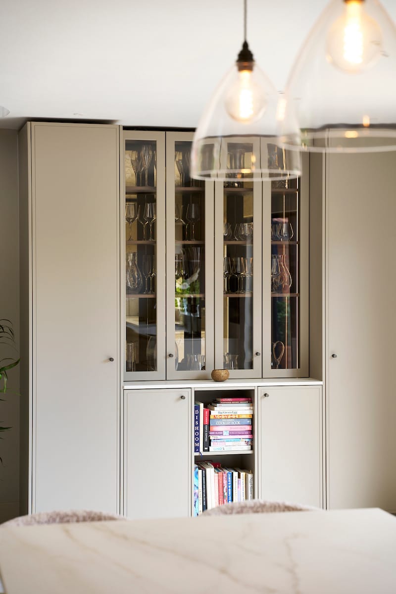 Close-up of a glass-fronted display cabinet with oak interior shelving in a modern Essex kitchen.