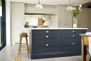 Elegant two-tone shaker kitchen with a deep blue island, brushed nickel cup handles, pale grey perimeter cabinetry, and industrial pendant lighting.