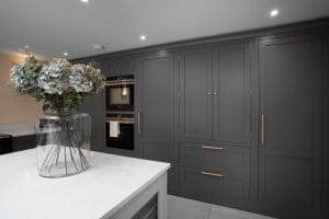Bespoke dark grey shaker-style kitchen cabinetry with integrated appliances and brushed brass handles, paired with a white marble-effect quartz island.