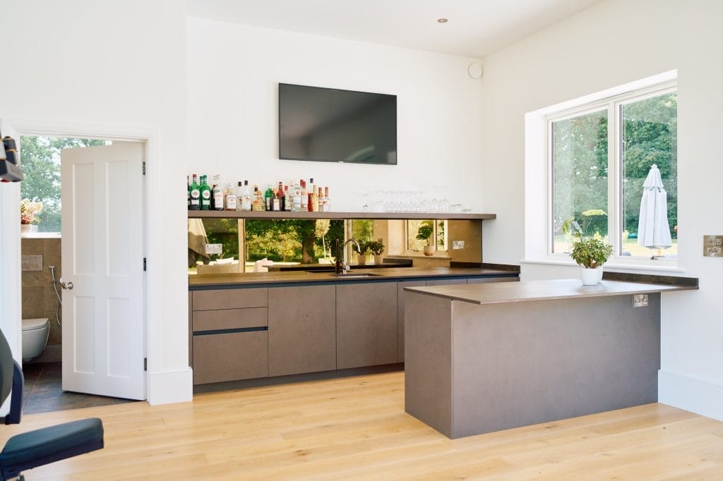 Minimalist Handleless Kitchen Essex home bar with matte taupe cabinetry, bronze mirrored splashback, undermount sink and oak flooring.