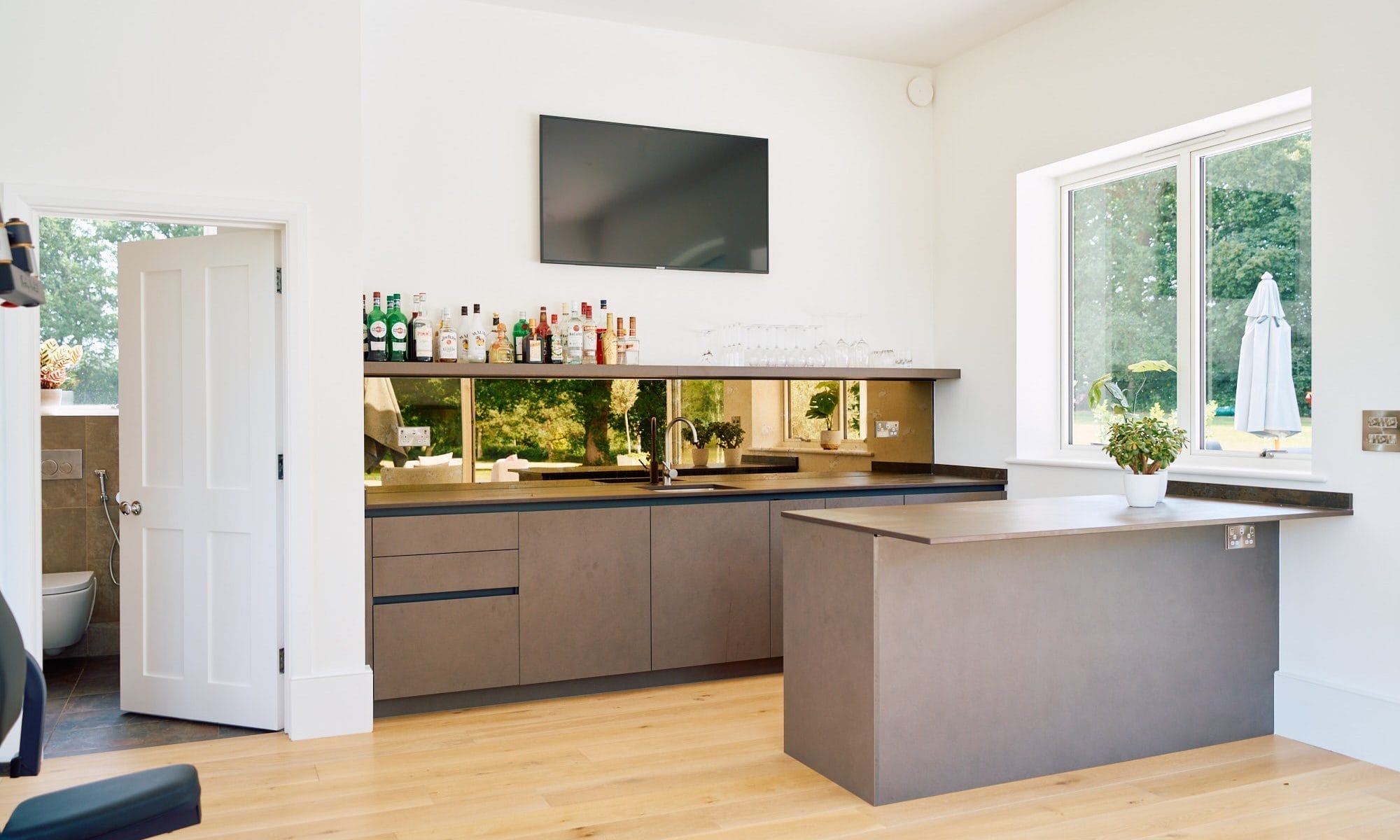 Minimalist Handleless Kitchen Essex home bar with matte taupe cabinetry, bronze mirrored splashback, undermount sink and oak flooring.
