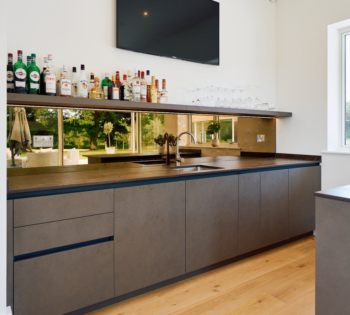 Close view of contemporary home bar showing bronze mirror back panel, bottle display shelf and integrated sink.