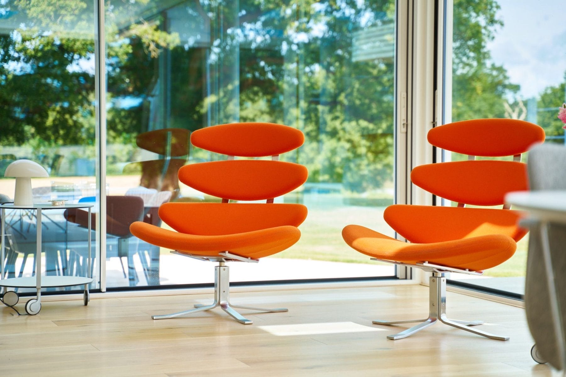 Pair of sculptural orange modern lounge chairs in front of floor‑to‑ceiling glass in a Minimalist handleless kitchen Essex home.