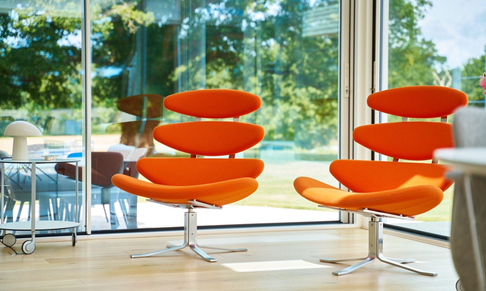 Pair of sculptural orange modern lounge chairs in front of floor‑to‑ceiling glass in a Minimalist handleless kitchen Essex home.