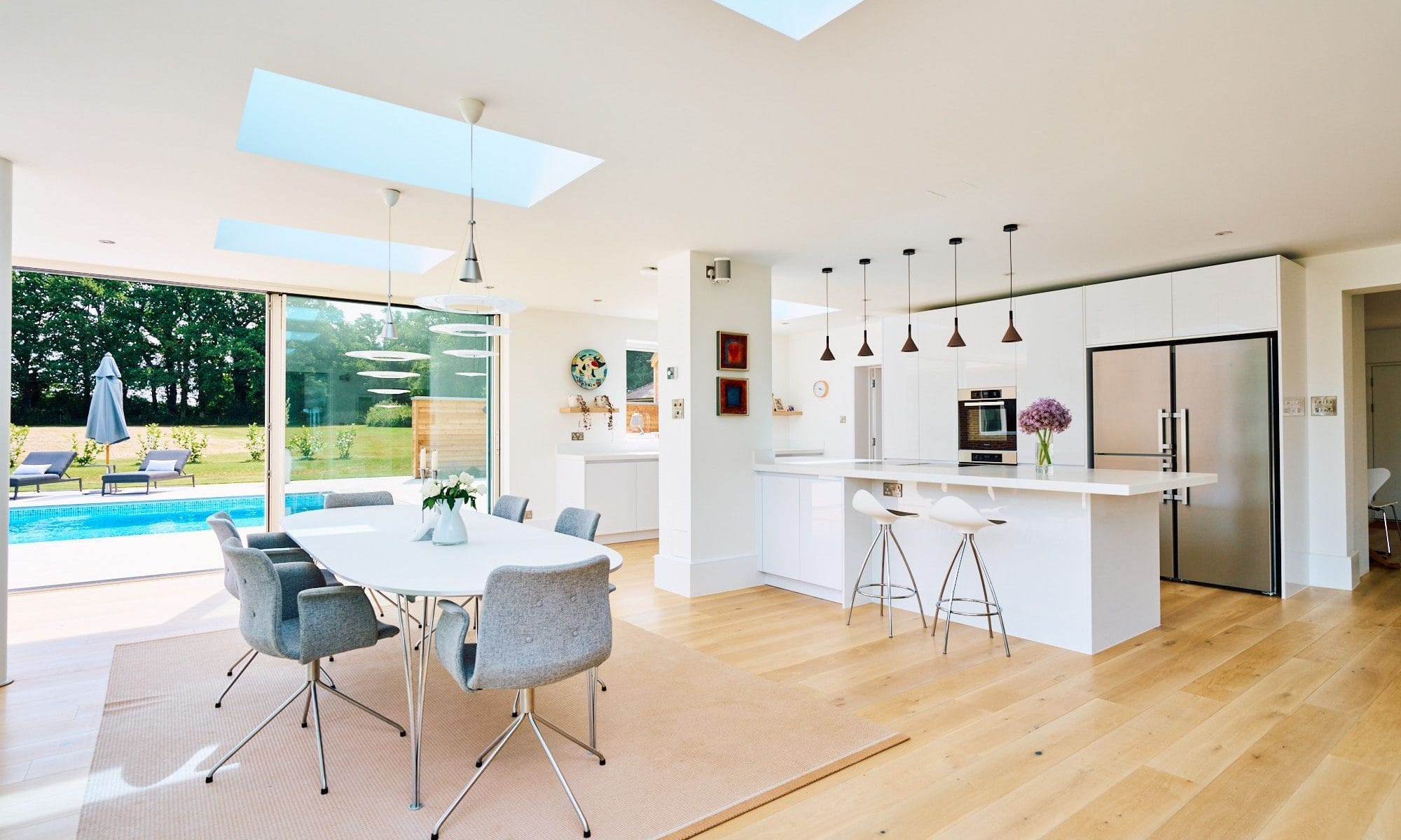 Open‑plan Minimalist handleless kitchen and dining space with sliding glass doors to pool terrace and countryside views.