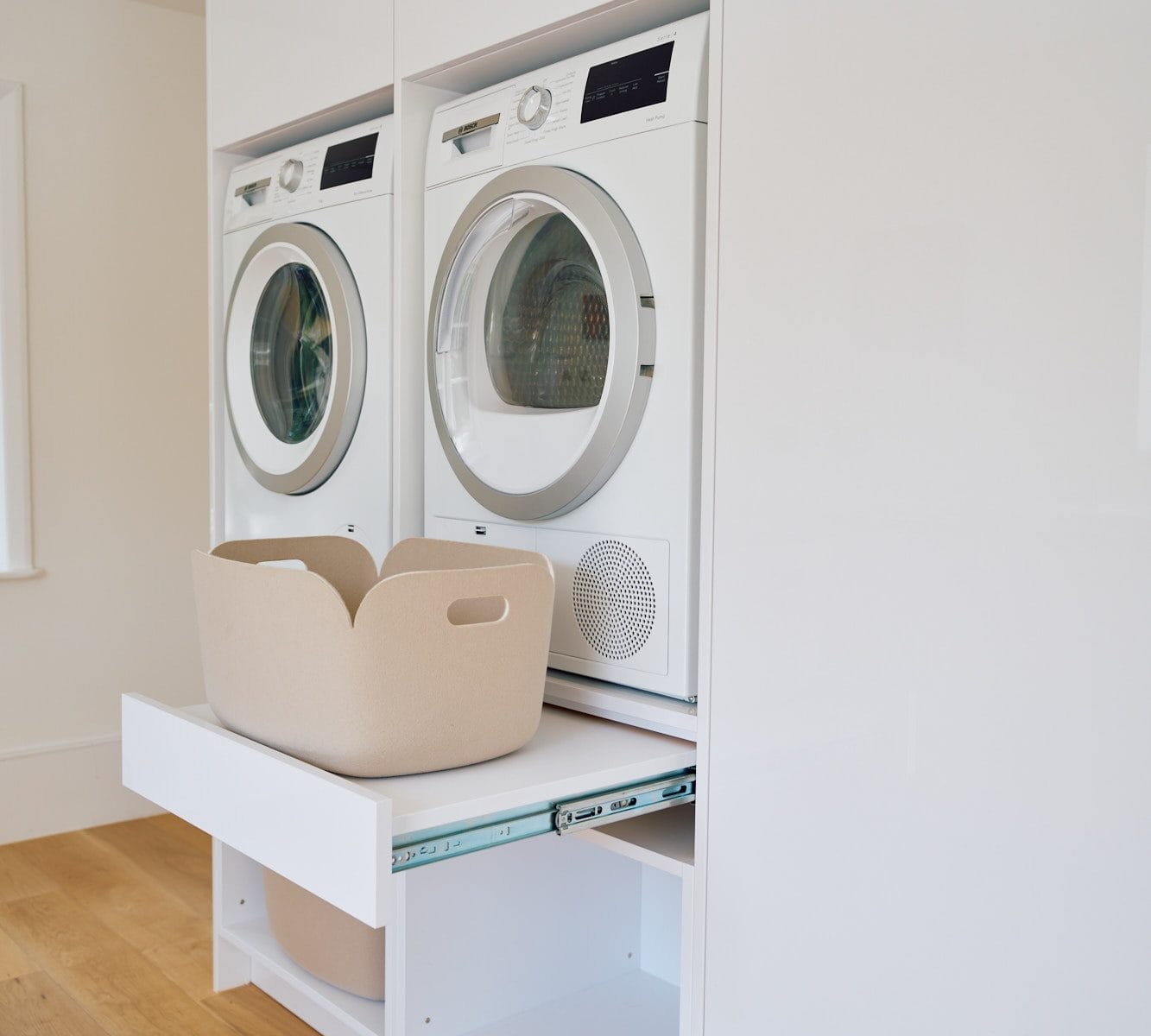 Minimalist handleless kitchen, Pull‑out laundry platform beneath stacked washer and dryer in a white utility room.